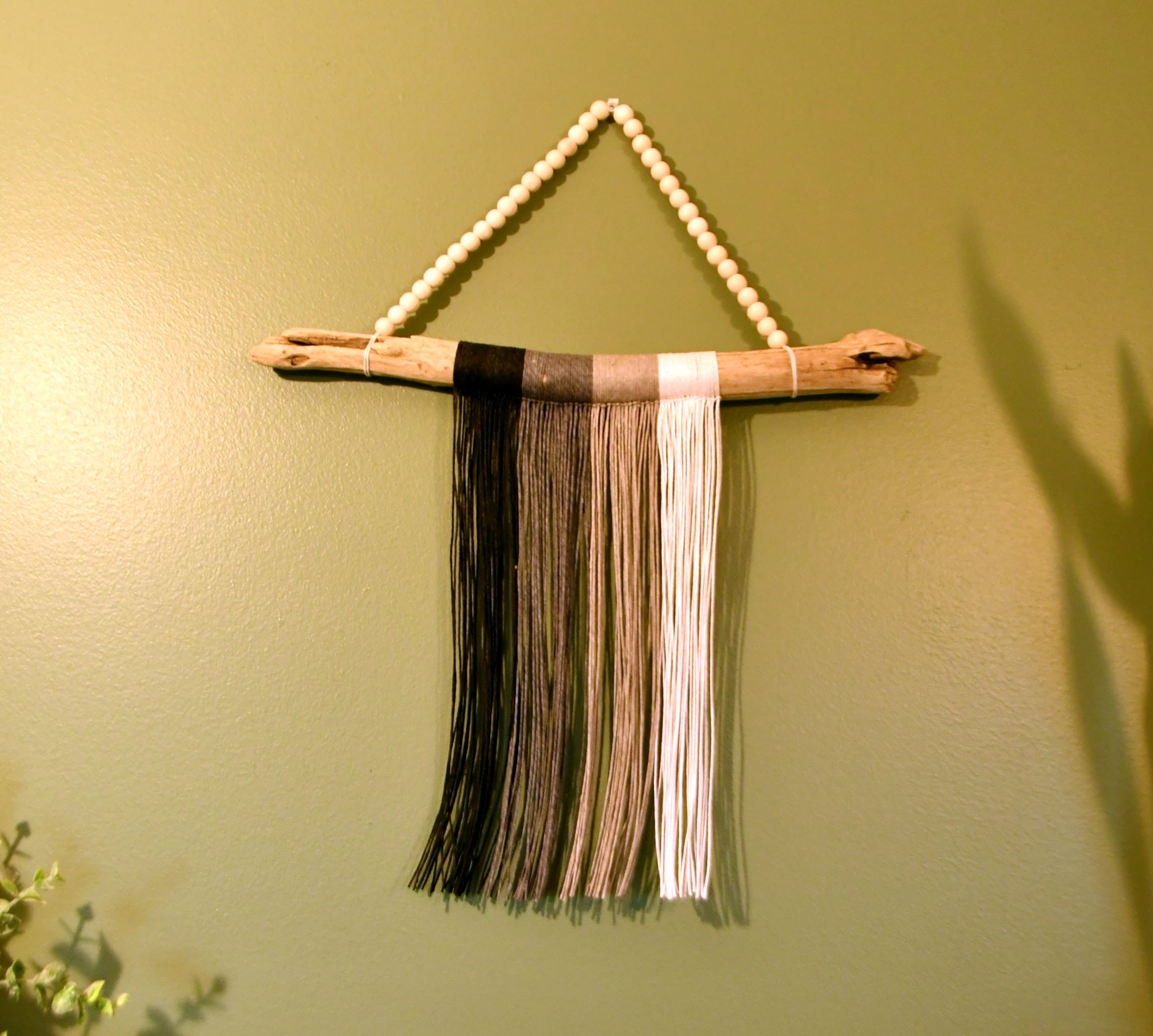 Decorative wall hanging with wooden sticks and colorful fringe on a green wall.